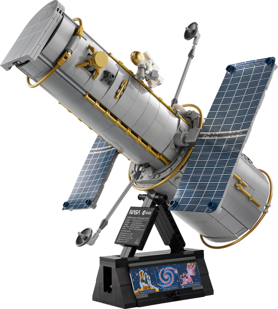 The LEGO Icons 11382 Hubble Space Telescope model on its black display stand, solar arrays extended, an astronaut minifigure attached to the silver barrel, and three brick-built Hubble images printed on the base.